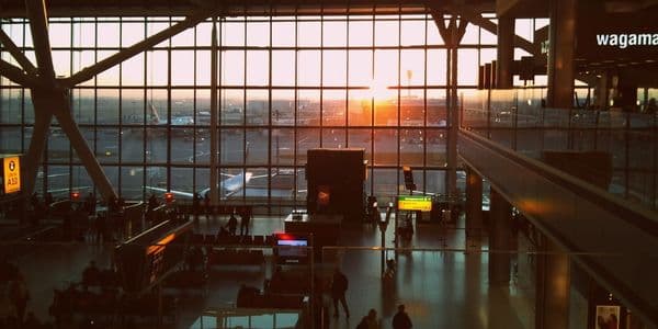 People inside an airport terminal while the sun is rising outside and shining in through the building's glass facade