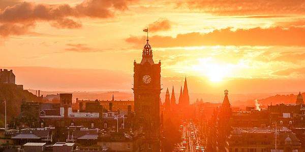 The golden light of the setting sun illuminates Edinburgh's city centre with the Balmoral Hotel in the foreground